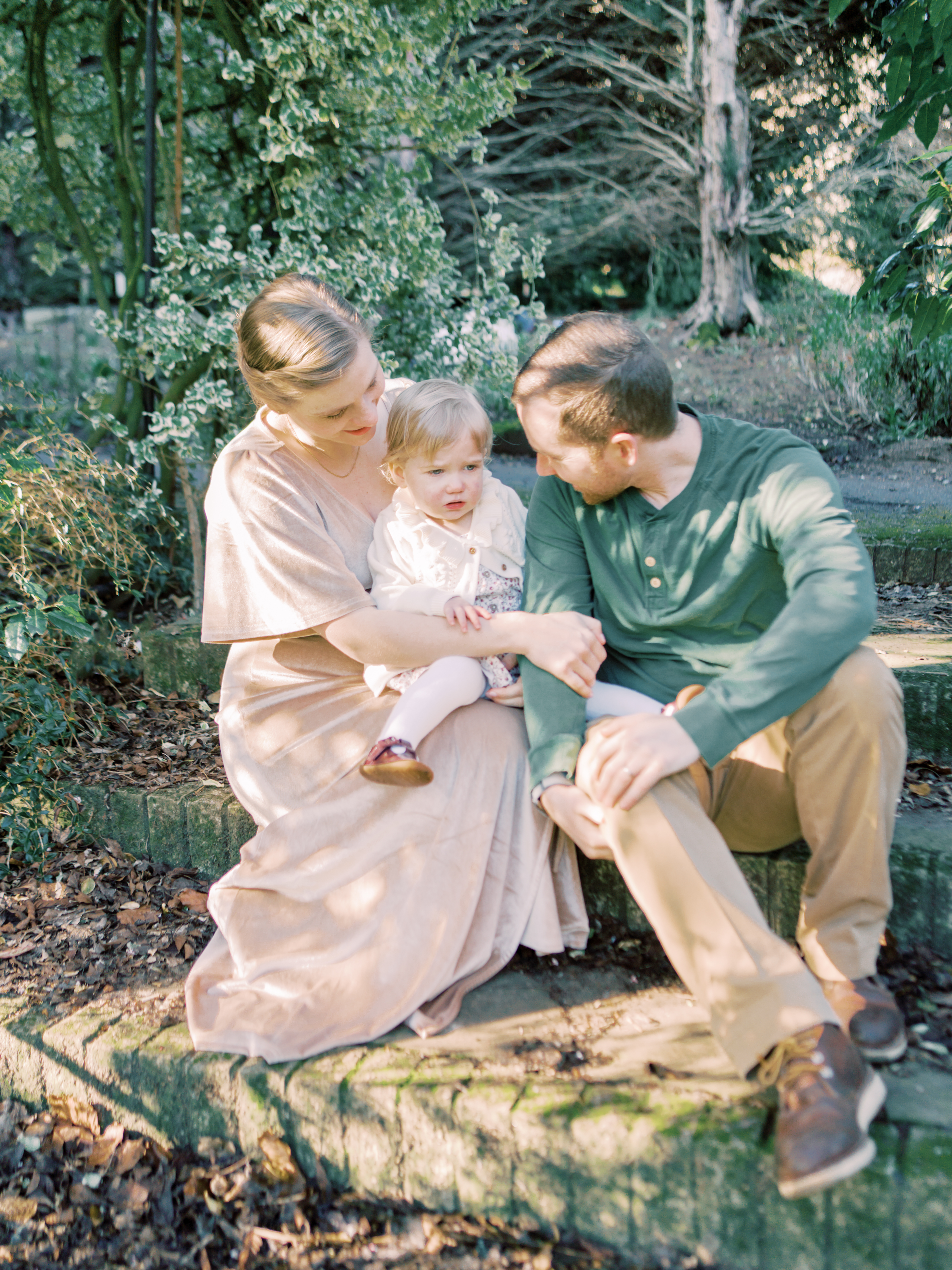 Family of three sits on steps in ancient and beautiful gardens during their professional family photo session