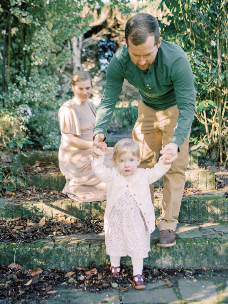 Dad helps daughter climb stairs in a beautiful garden environment during professional family photo session
