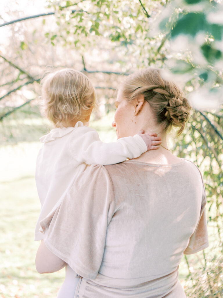 Mother holds daughter and has intimate moment where they explore arching vines in a garden during their professional family photo session.