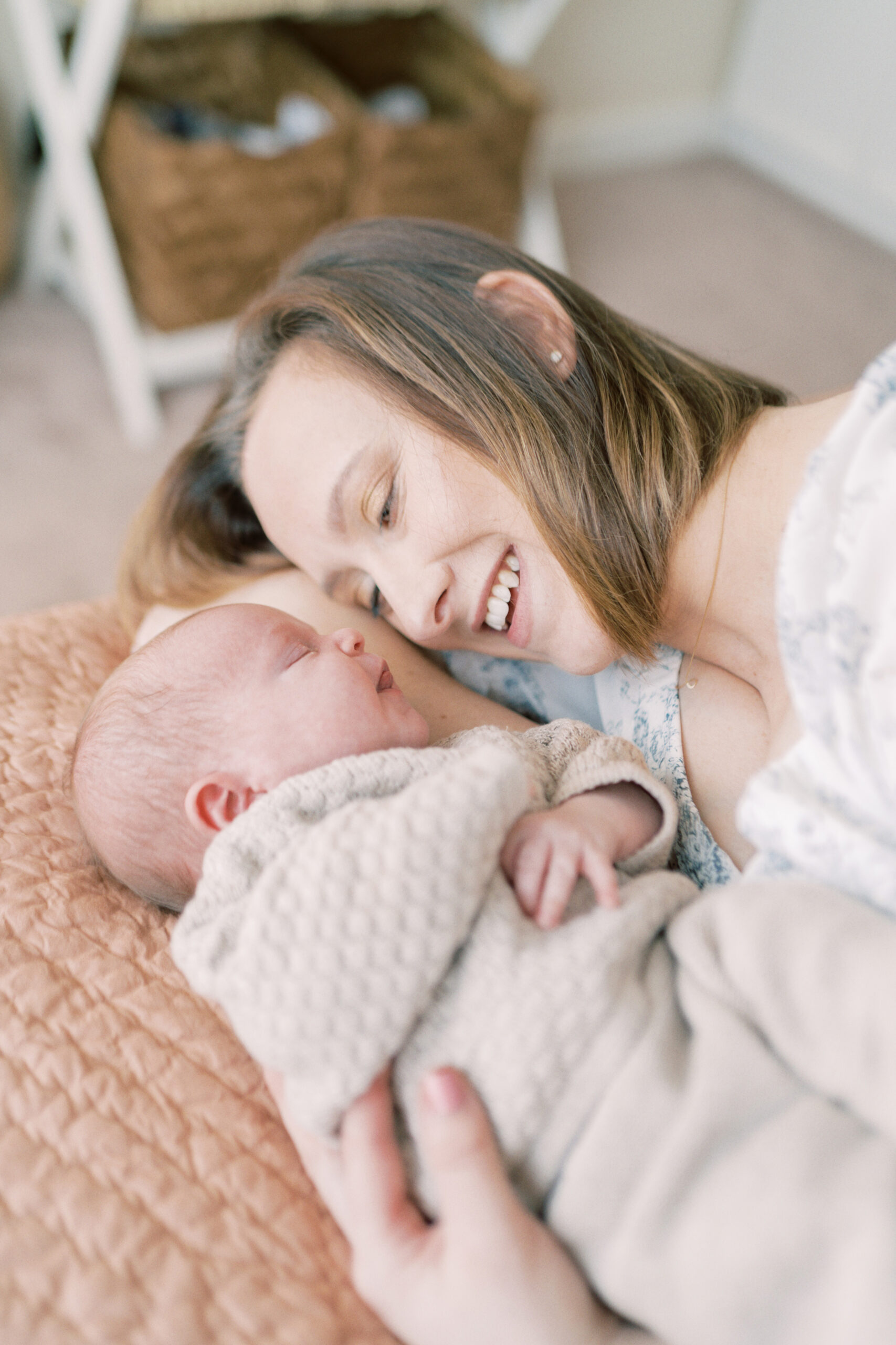 Mother cuddles next to her newborn daughter laying on her bed and stares lovingly at her during their newborn photo session by Courtney Cronin photography in Oklahoma