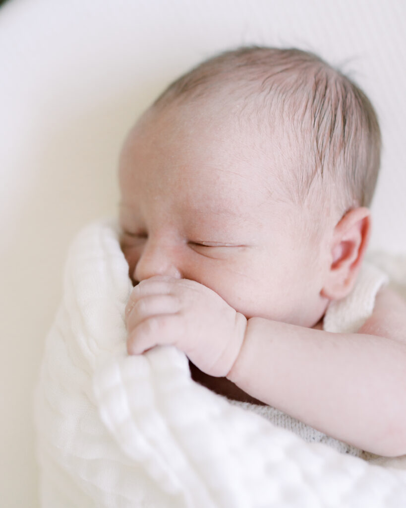 Newborn baby snuggles into his white blanket by Newborn Photographer Courtney Cronin