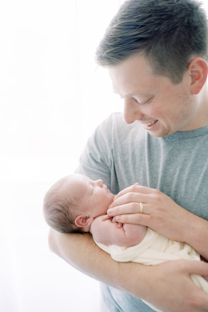 Backlit photo of father holding newborn baby boy and smiling at him by Lawton Ok photographer Courtney Cronin