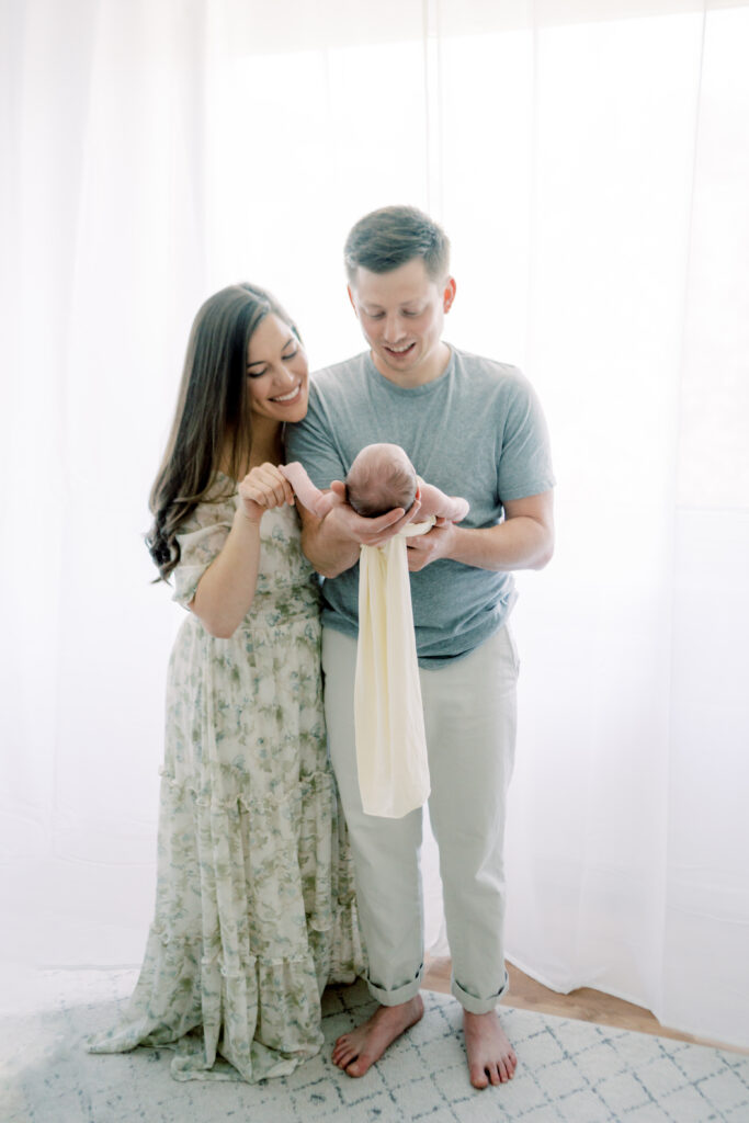 Mother plays with newborn's hand while father holds him during their newborn photo shoot by OKC newborn photographer Courtney Cronin