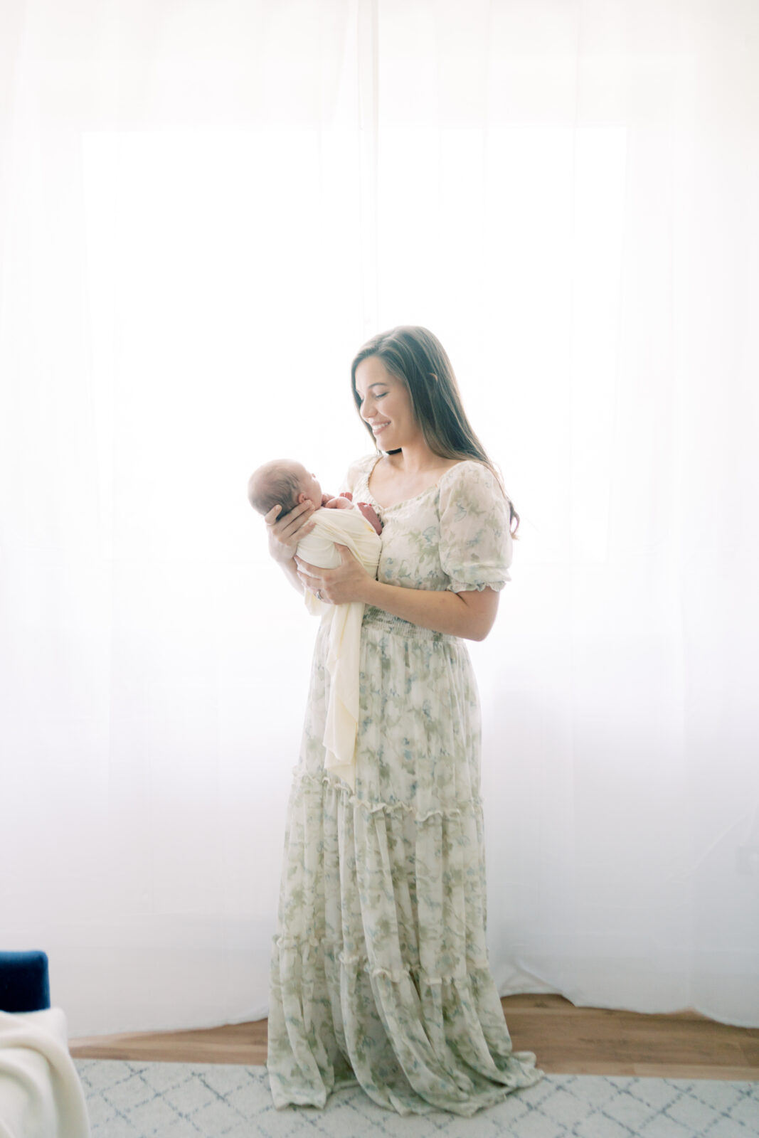 Backlit photo of mother in a flowy dress holding her newborn baby boy and looking down at him while singing to him by Lawton Ok photographer Courtney Cronin