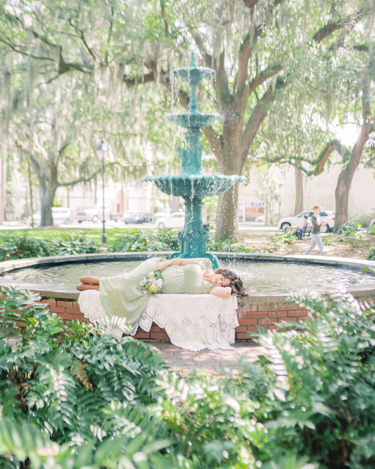 Pregnant mother lays on rim of fountain at Lafayette Square enjoying the sunlight by Savannah Family Photographer Courtney Cronin