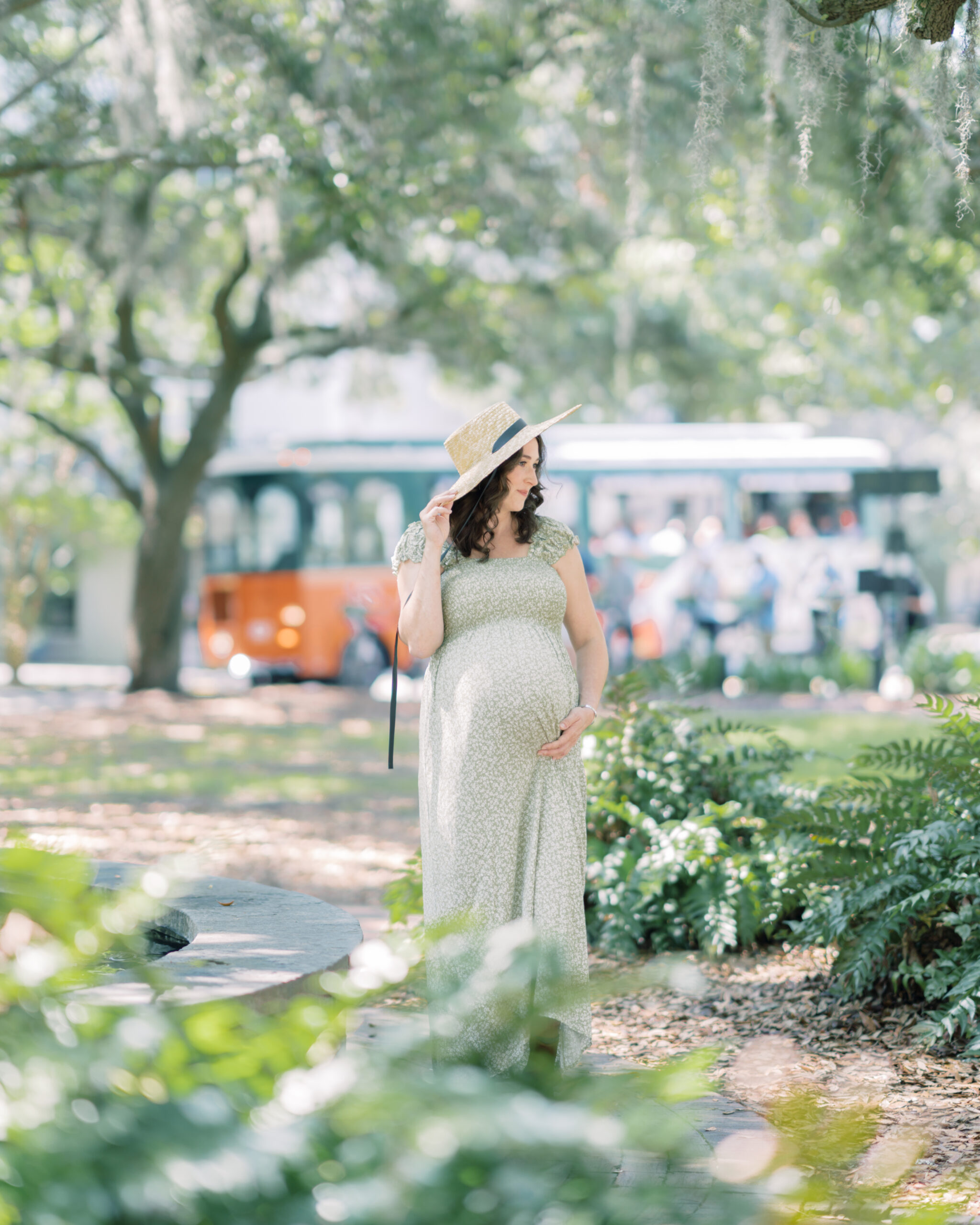Mother hold hat down while standing in front of Savannah's iconic tour trolleys in Lafayette Square by Savannah Family Photographer Courtney Cronin